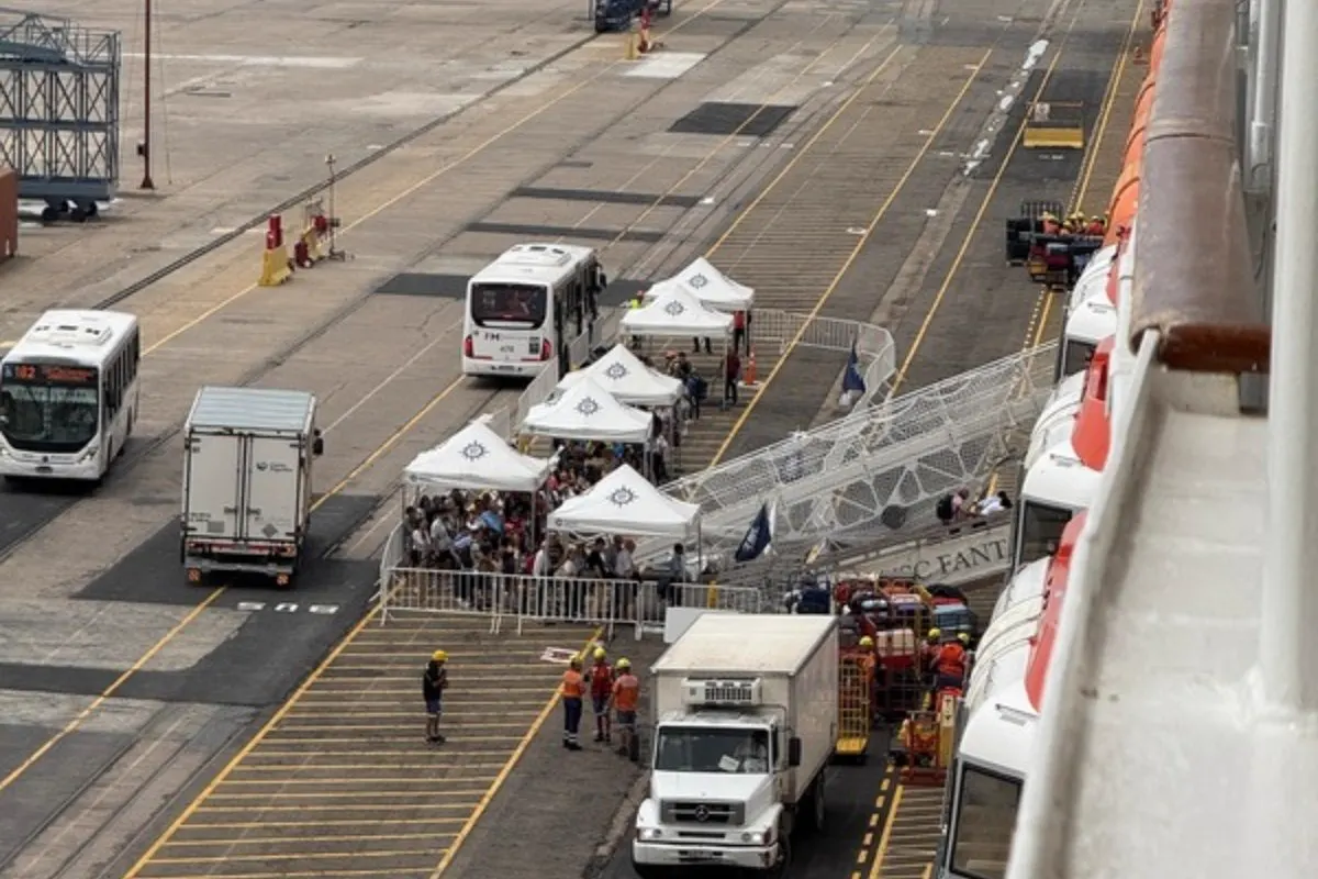 Pasajeros haciendo fila bajo carpas en el muelle, junto al barco, para embarcar