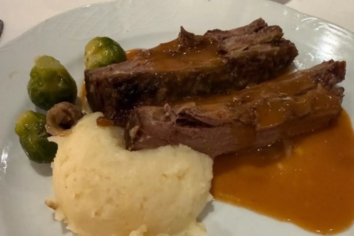 Plato de carne con salsa, puré y coles de Bruselas en el restaurante principal de un crucero