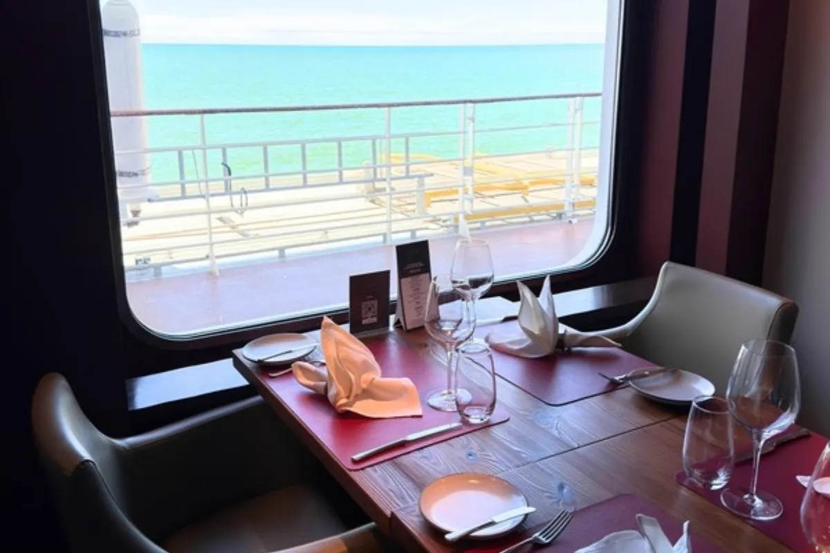 Mesa servida junto a una ventana con vista al mar en un restaurante de especialidad de un crucero