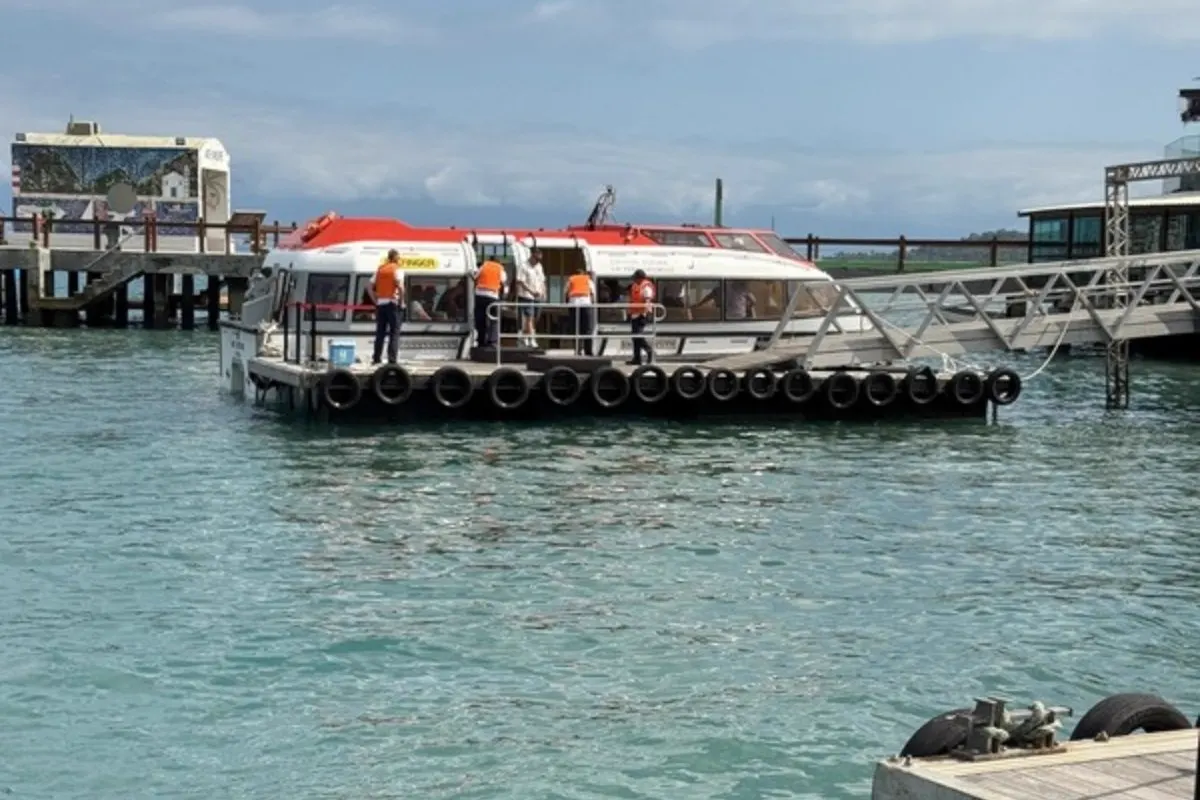 Lancha tender con tripulantes en uniforme naranja amarrada en un muelle
